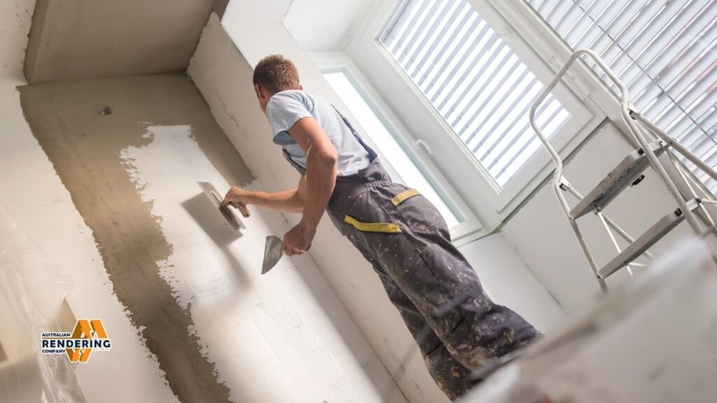 Man plastering wall with trowel near ladder and window